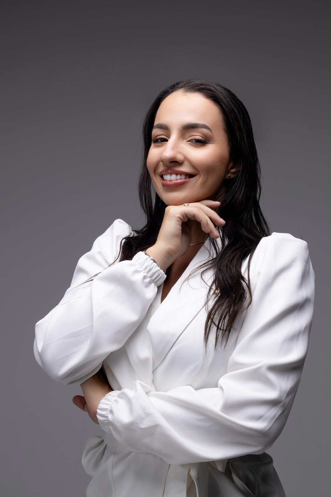 Dra. Isabela sorrindo, com a mão apoiada no queixo e blazer branco.