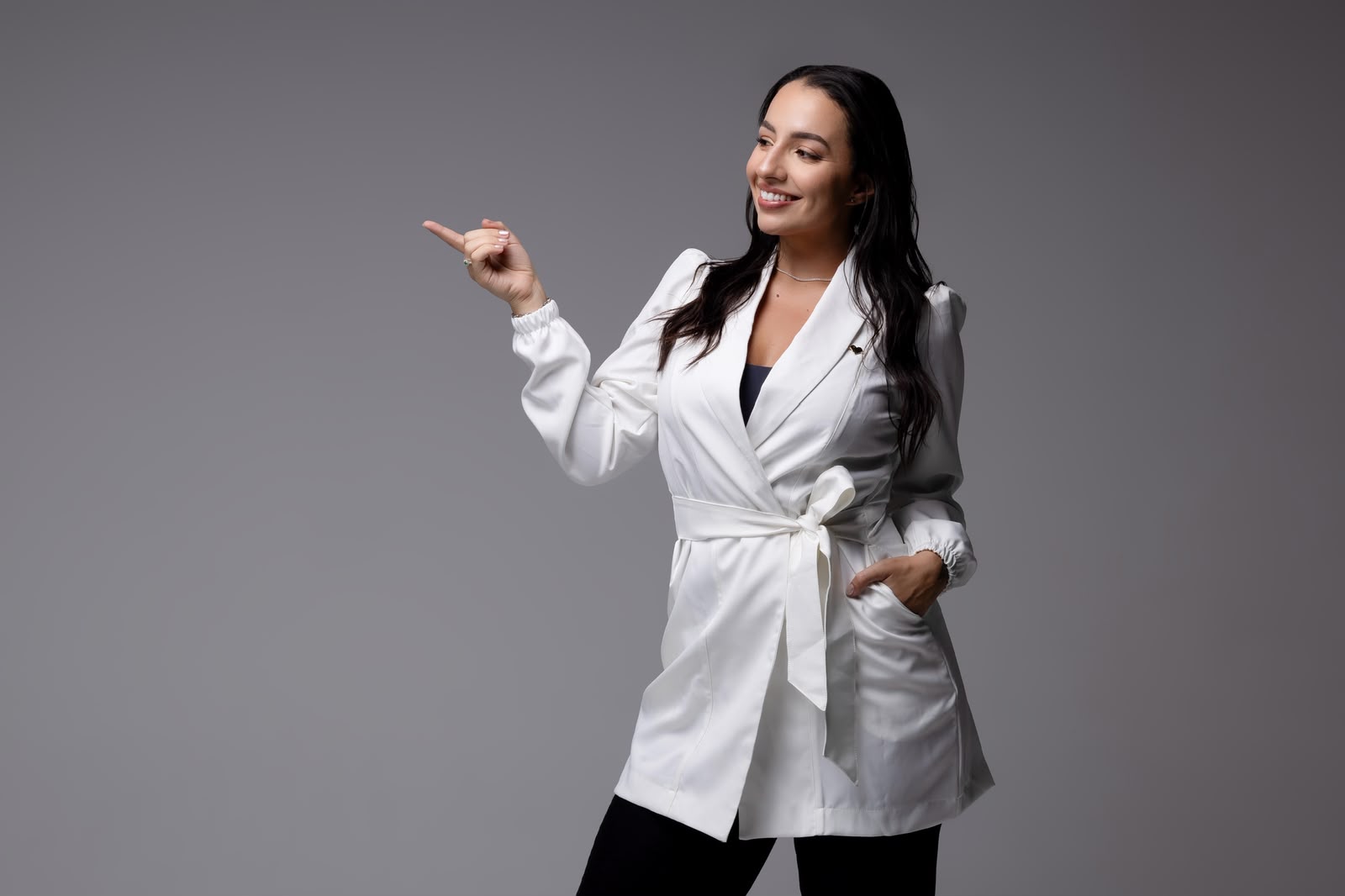 Dra. Isabela de blazer branco, apontando para o lado.